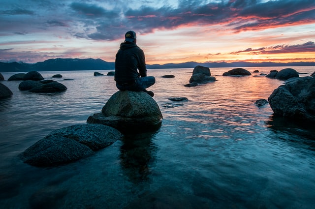 person sitting on a rock looking at a sunset scene